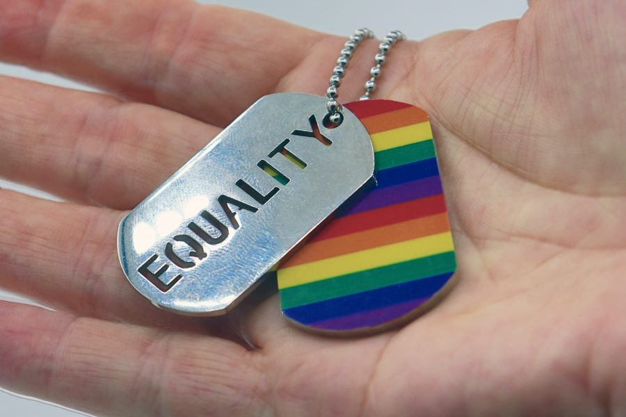 Hand holding Rainbow and Equality dog tags on a chain
